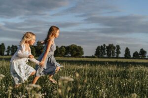 Two happy young sisters running hand in hand through a sunlit meadow.